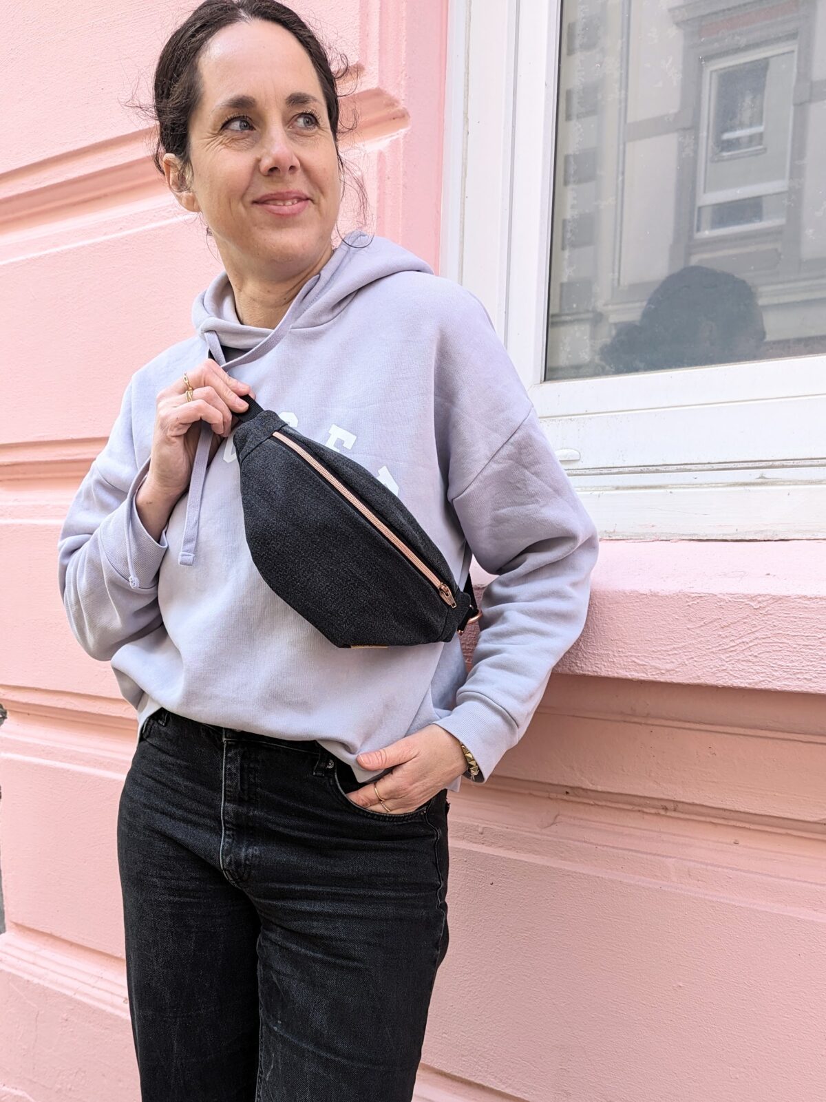 Frau mit Kapuzenpullover trägt eine schwarze Bauchtasche aus jeans